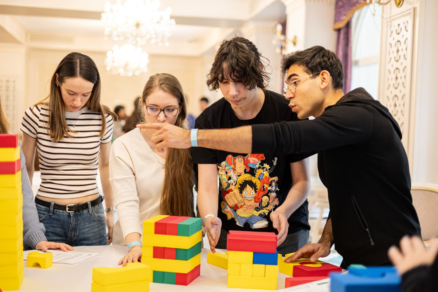 Patru studenți construiesc împreună un turn din cuburi colorate, la teambuildingul din noiembrie 2025
